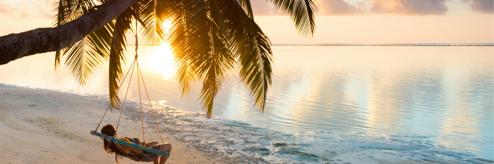 Maldives at sunset. Hammock on the beach attached to a palm tree
